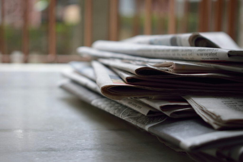 A close-up of a stack of newspapers resting on a desk, symbolizing information and media.